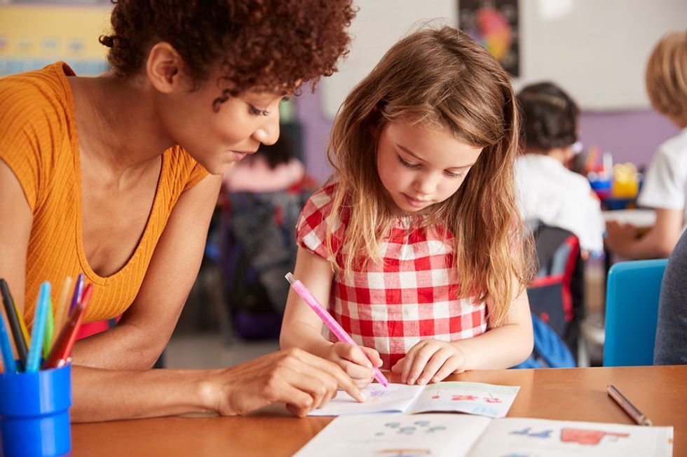 Elementary school teacher helps her student color in pictures